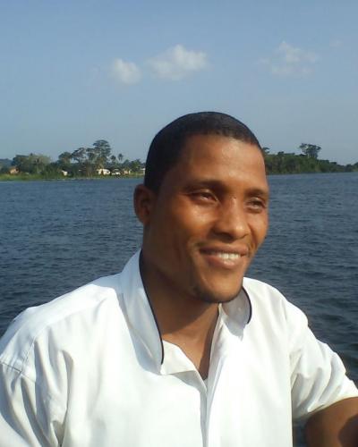 A man in a white shirt smiles while sitting in front of a large body of water.