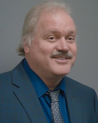 A man in a blue suit and tie smiles while looking off to the side.