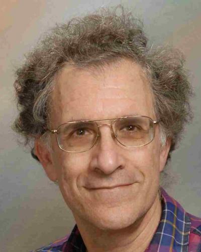 A man with short, curly hair and glasses smiles at the camera.