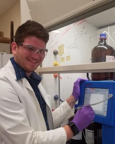 A man wearing a white lab coat and purple gloves works with a piece of equipment in a laboratory setting.